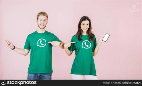 couple with cellphone pointing their t shirt with whatsapp icon