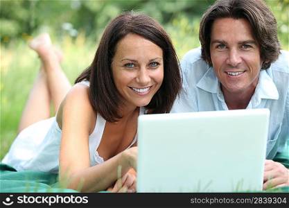 Couple with computer lying in the grass