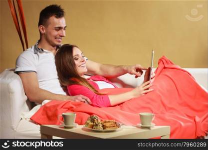Couple with credit card shopping online by tablet.. Couple with credit card shopping online Woman and man laying on sofa at home using new technology to buy.