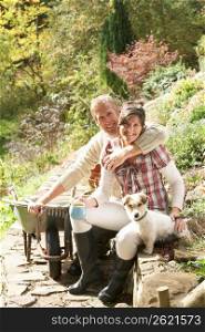 Couple With Dog Having Coffee Break Whilst Working Outdoors In Garden