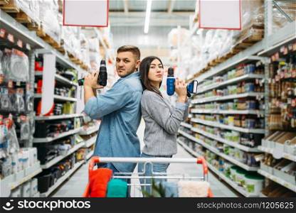 Couple with electric screwdrivers, power tools department in supermarket, family shopping. Customers in shop, buyers choosing consumer goods