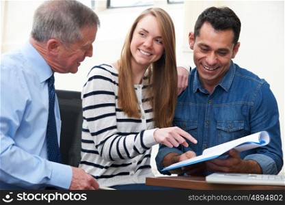 Couple With Financial Advisor Studying Document In Office