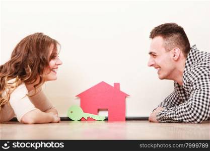 Couple with paper house. Housing real estate.. Smiling young couple laying on floor holding paper house and key. Husband and wife dreaming about new home. Housing and real estate concept.