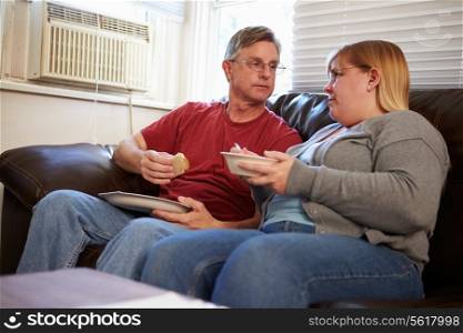 Couple With Poor Diet Sitting On Sofa Eating Meal