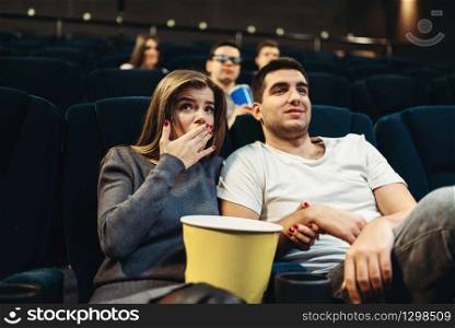 Couple with popcorn fascinated watching the film in cinema. Showtime, entertainment industry. Couple fascinated watching the film in cinema