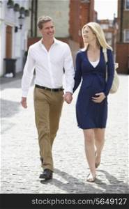 Couple With Pregnant Wife Walking Along Urban Sidewalk