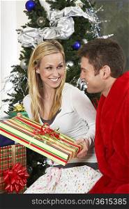 Couple with present by Christmas tree