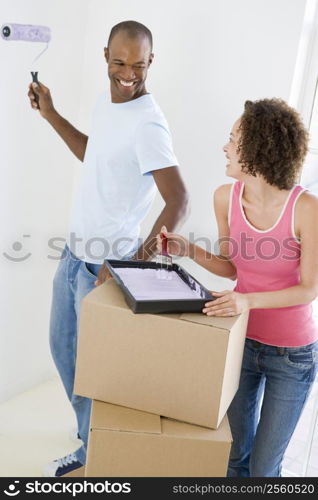 Couple with roller and paint in new home smiling