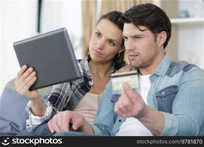 couple with tablet pc and credit card on sofa