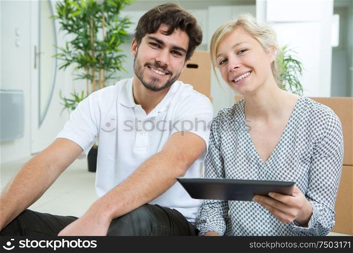 couple with tablet sitting on floor at new apartment