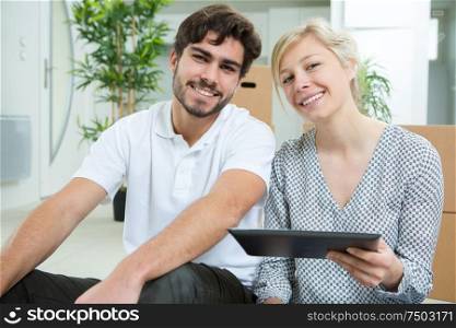 couple with tablet sitting on floor at new apartment