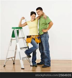 Couple with tools and ladder standing in home smiling.