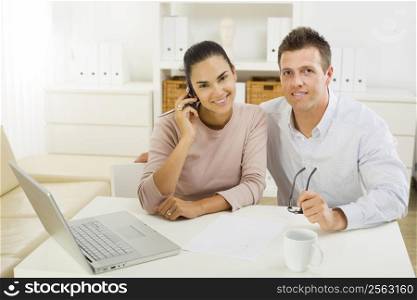 Couple working on laptop computer at home office, happy, smiling.