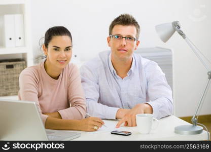 Couple working on laptop computer at home office, happy, smiling.