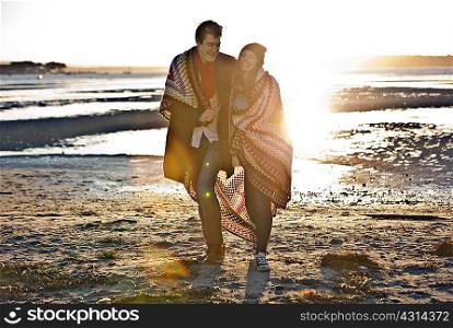 Couple wrapped in a blanket walking on the beach