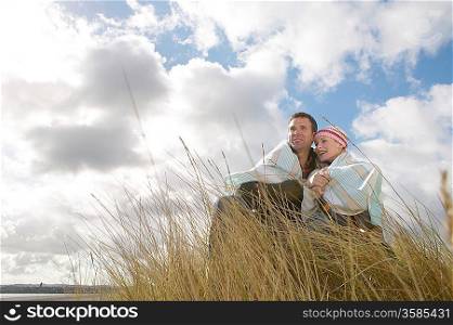 Couple wrapped in blanket embracing in grass