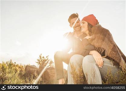 Couple wrapped in blanket sitting on rock in field
