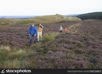 Couples Hiking Across Moorland Covered With Heather