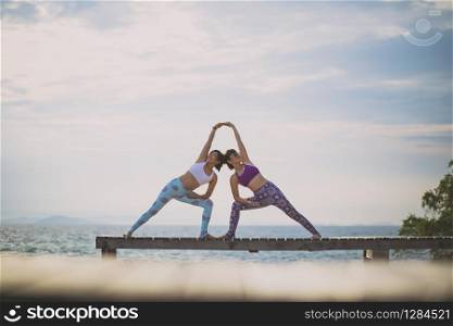 couples of woman playing yoga pose on beach pier with moring sun light