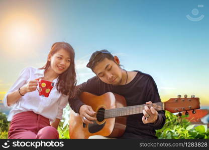 couples of younger asian man and woman relaxing playing guitar in park