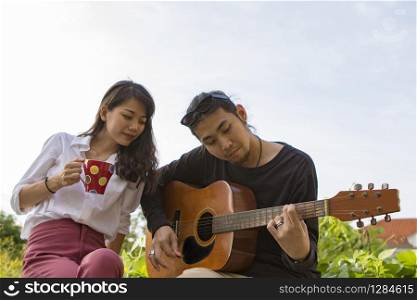 couples of younger asian man and woman relaxing playing guitar in park