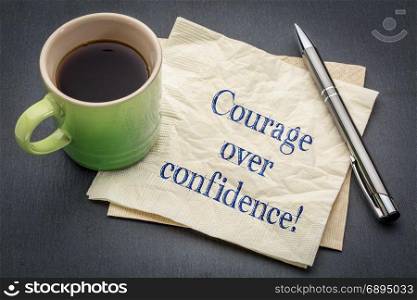 Courage over confidence! Handwriting on a napkin with cup of coffee against gray slate stone background