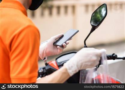 Courier deliveryman with face mask and glove on motorbike or motorcycle check customer location by smartphone. New normal of food delivery business during covid19 or coronavirus pandemic concept.