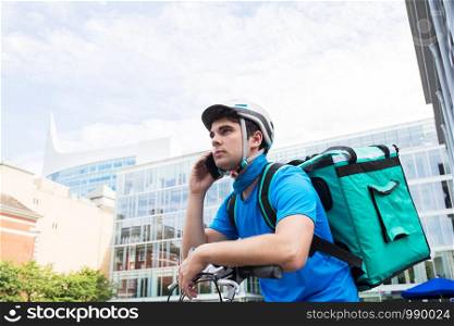 Courier On Bicycle Delivering Food In City Using Mobile Phone