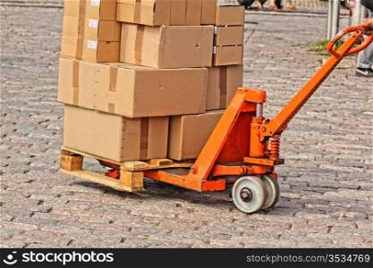 Courier shipping carboard boxes on a orange trolly, on stone floor