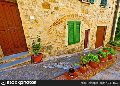 Courtyard with old buildings in the medieval italian town. Entrance to the tuscan home decorated with flowers in Italy