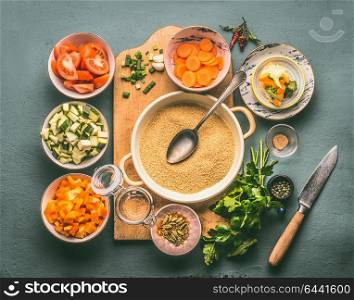 Couscous and vegetarian cooking ingredients in bowls on cutting board with spoon , gray background, top view