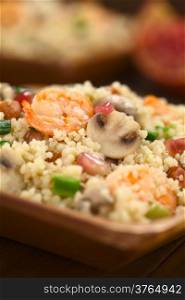 Couscous dish with shrimps, mushroom, almond, pomegranate seeds and green onion served on wooden plate (Selective Focus, Focus on the tail of the shrimp on the top of the meal and on the upper part of the mushroom slice next to it)