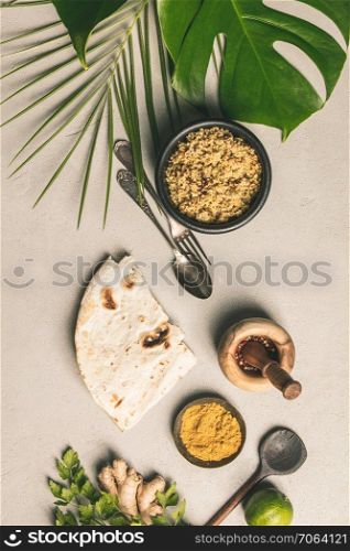 Couscous, green leaf and cooking ingredients on concrete background. Flat lay. Healthy vegetarian food and cooking concept