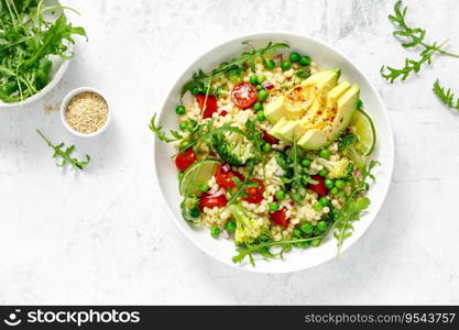 Couscous salad with broccoli, green peas, tomatoes, avocado and fresh arugula. Healthy natural plant based vegetarian food for lunch, israeli cuisine, top view