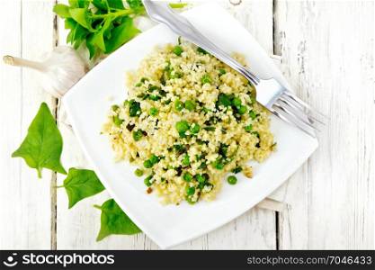 Couscous with spinach and green peas in a plate on a kitchen towel, basil and fork on a wooden plank background