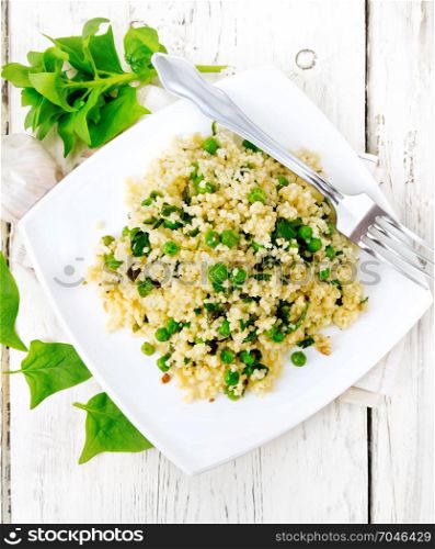 Couscous with spinach and green peas in a plate on a towel, basil and fork on a wooden plank background