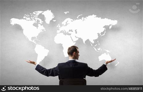 Cover the whole world. Businessman sitting in chair and cover world map with hands