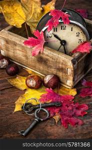 covered with autumn leaves old alarm clock in wooden box on the table. autumn leaf fall