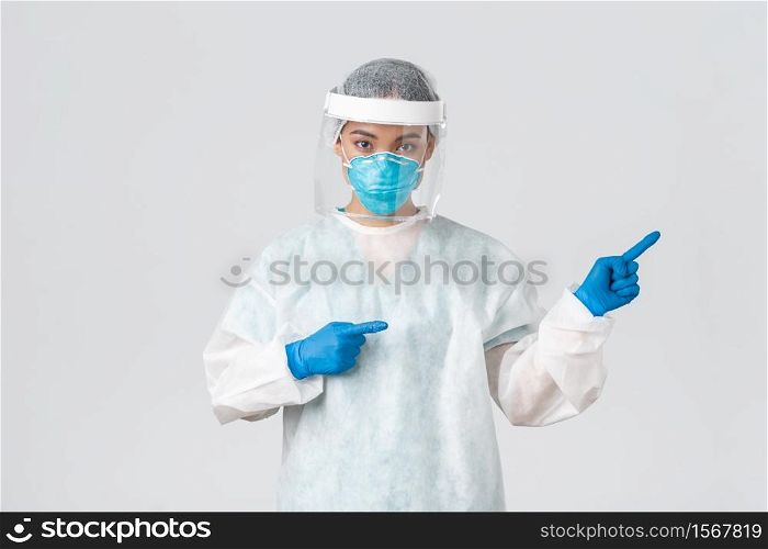 Covid-19, coronavirus disease, healthcare workers concept. Professional female doctor, tech lab employee in personal protective equipment pointing fingers right, showing way, white background.. Covid-19, coronavirus disease, healthcare workers concept. Professional female doctor, tech lab employee in personal protective equipment pointing fingers right, showing way, white background