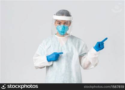 Covid-19, coronavirus disease, healthcare workers concept. Professional female doctor, tech lab employee in personal protective equipment pointing fingers right, showing way, white background.. Covid-19, coronavirus disease, healthcare workers concept. Professional female doctor, tech lab employee in personal protective equipment pointing fingers right, showing way, white background