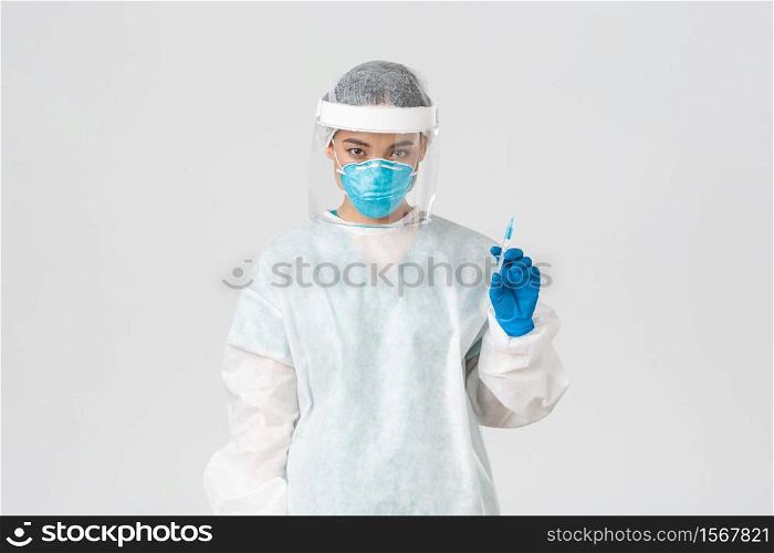 Covid-19, coronavirus disease, healthcare workers concept. Serious-looking confident asian female doctor in medical respirator and personal protective equipment, holding syringe with vaccine.. Covid-19, coronavirus disease, healthcare workers concept. Serious-looking confident asian female doctor in medical respirator and personal protective equipment, holding syringe with vaccine