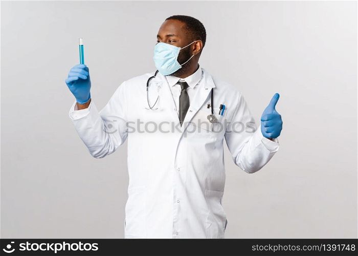 Covid-19, coronavirus patient treatment and laboratory concept. Satisfied african-american doctor invented virus vaccine, delighted looking at vial, test-tube with blue liquid, show thumbs-up.. Covid-19, coronavirus patient treatment and laboratory concept. Satisfied african-american doctor invented virus vaccine, delighted looking at vial, test-tube with blue liquid, show thumbs-up