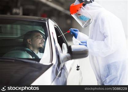 COVID-19 drive-thru rt-PCR detection site,medical worker performing nasal swab specimen collection on young male driver,free Coronavirus public diagnostic procedure,mobile car testing center clinic