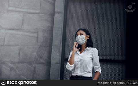 Covid-19 or Corona Virus Situation in Business Concept. Business Woman with Medical Mask Looking Up while Using Smartphone. Face with a Deep Concern. Dark Wall Office Building as background