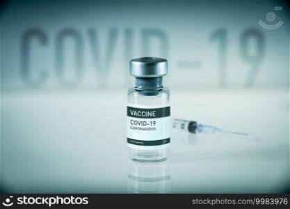 Covid-19 vaccine bottle and syringe on a blue laboratory background. Covid-19 vaccine bottle and syringe on a blue background