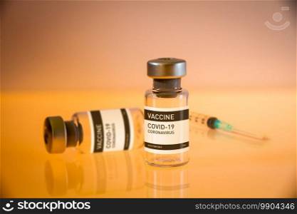 Covid-19 vaccine bottle and syringe on a yellow laboratory background. Covid-19 vaccine bottle and syringe on a yellow background