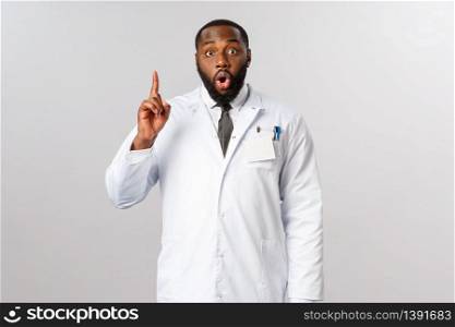 Covid19, healthcare and clinic concept. African american male doctor, physician have great idea, raise finger up eureka sign, gasping, saying his suggestion, explain plan or usage of medical masks.. Covid19, healthcare and clinic concept. African american male doctor, physician have great idea, raise finger up eureka sign, gasping, saying his suggestion, explain plan or usage of medical masks