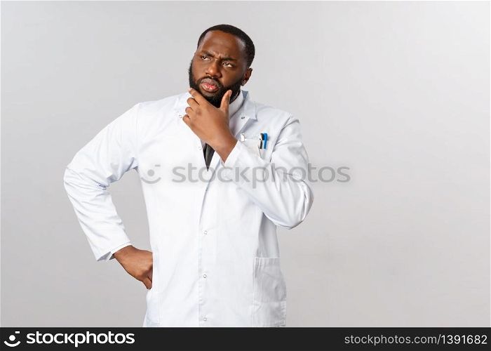 Covid19, healthcare and clinic concept. African-american male doctor thinking about patient symptoms, look away serious, pondering important decision, prescribe treatment, stand thoughtful.. Covid19, healthcare and clinic concept. African-american male doctor thinking about patient symptoms, look away serious, pondering important decision, prescribe treatment, stand thoughtful