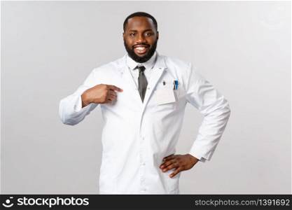 Covid19, healthcare and clinic concept. Portrait of confident handsome african-american doctor, pointing himself and smiling assured, tell contact your therapist or local hospital in case of disease.. Covid19, healthcare and clinic concept. Portrait of confident handsome african-american doctor, pointing himself and smiling assured, tell contact your therapist or local hospital in case of disease