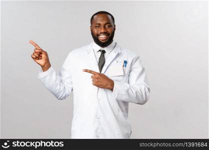 Covid19, healthcare and clinic concept. Portrait of handsome smiling african-american doctor in white coat inviting visit hospital for check-up, showing or pointing left, prescribe medicine.. Covid19, healthcare and clinic concept. Portrait of handsome smiling african-american doctor in white coat inviting visit hospital for check-up, showing or pointing left, prescribe medicine